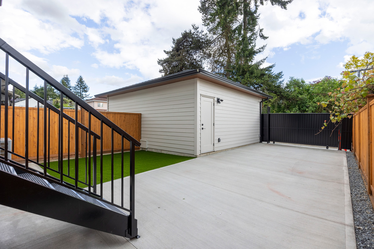 Concrete driveway next to a white garage with wooden fencing and black metal gate under a partly cloudy sky.