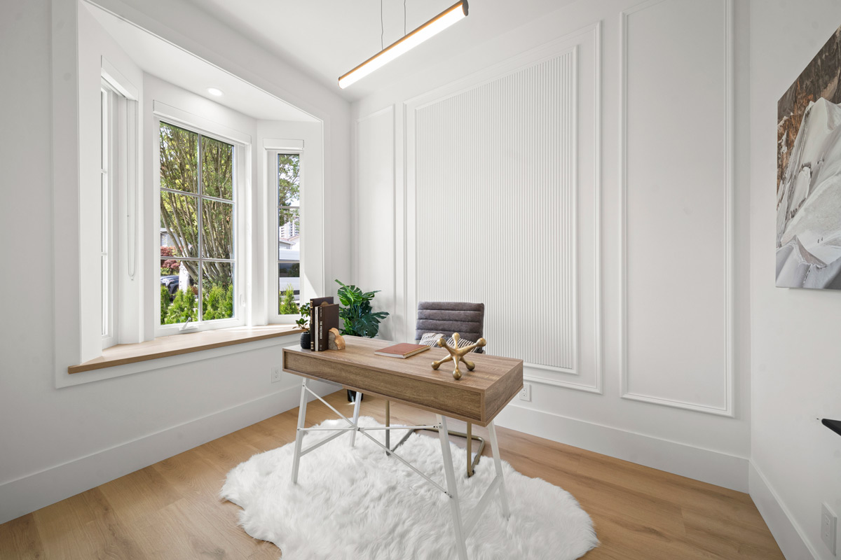 Built by Asthan Homes in Burnaby, BC, home office with wooden desk, gray chair, white fur rug, large bay window, and decorative wall panels.