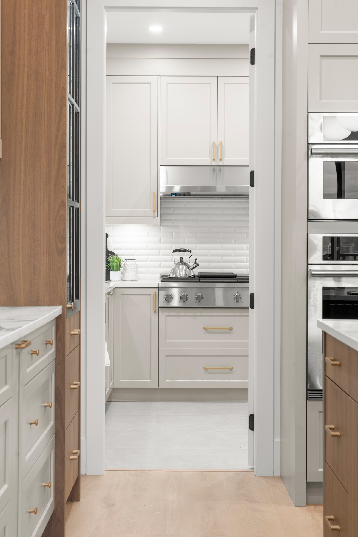 Built by Asthan Homes in Burnaby, BC, kitchen with white cabinets, stainless steel stove and hood, wooden drawers, and marble countertops.