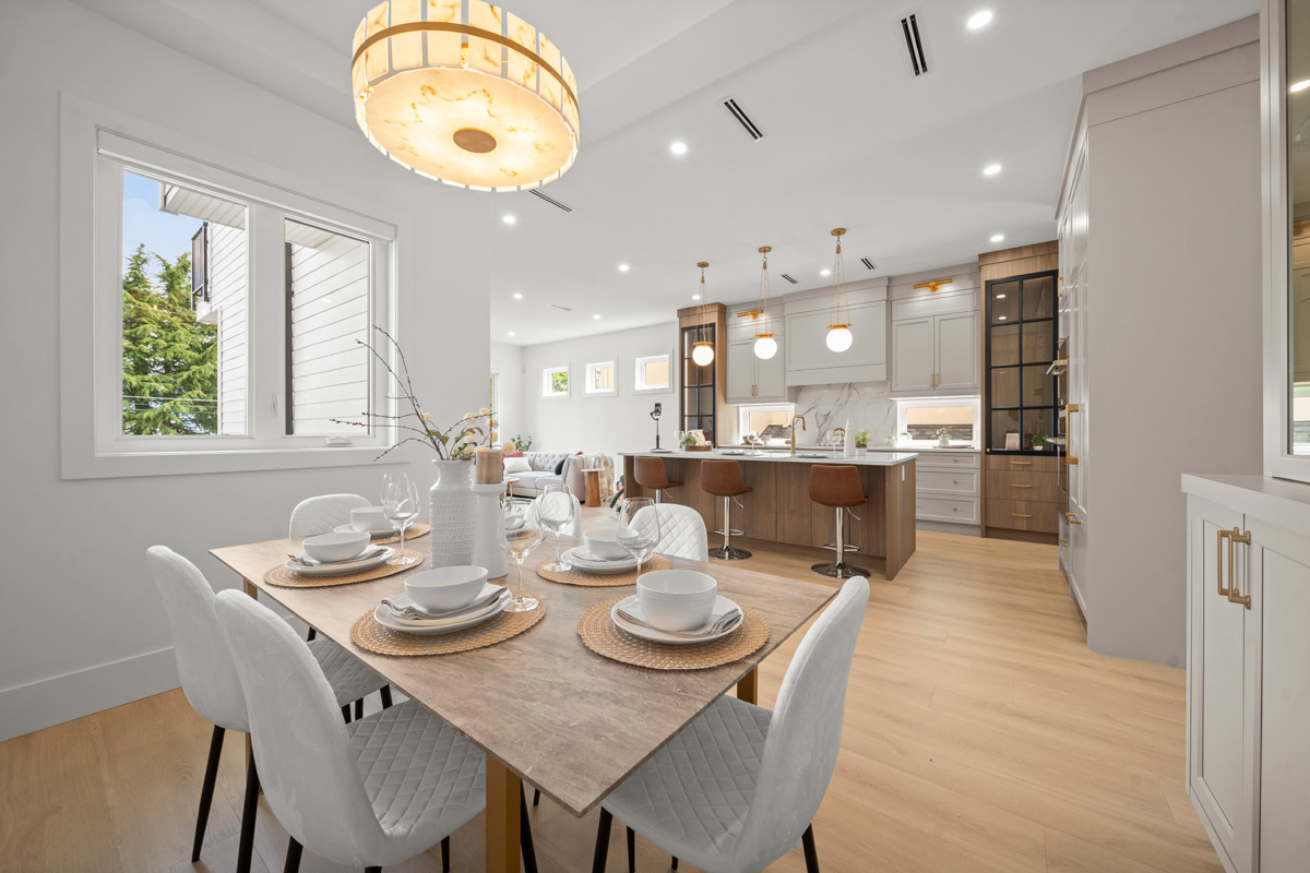 Built by Asthan Homes, modern dining area with a wooden table set for six and a kitchen island with brown bar stools in the background.