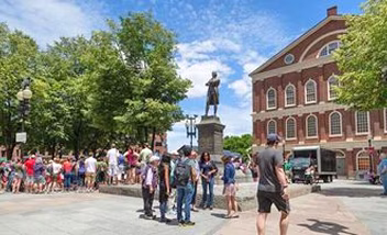 Visitors at a statue in a square with trees and buildings.