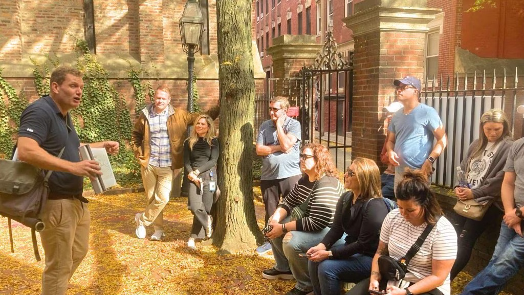 Tour guide leading an outdoor group near a historic brick building in autumn.