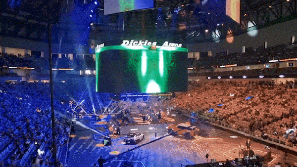 Indoor arena with a large crowd watching a live performance with bright stage lights and a central screen displaying Dickies Arena.