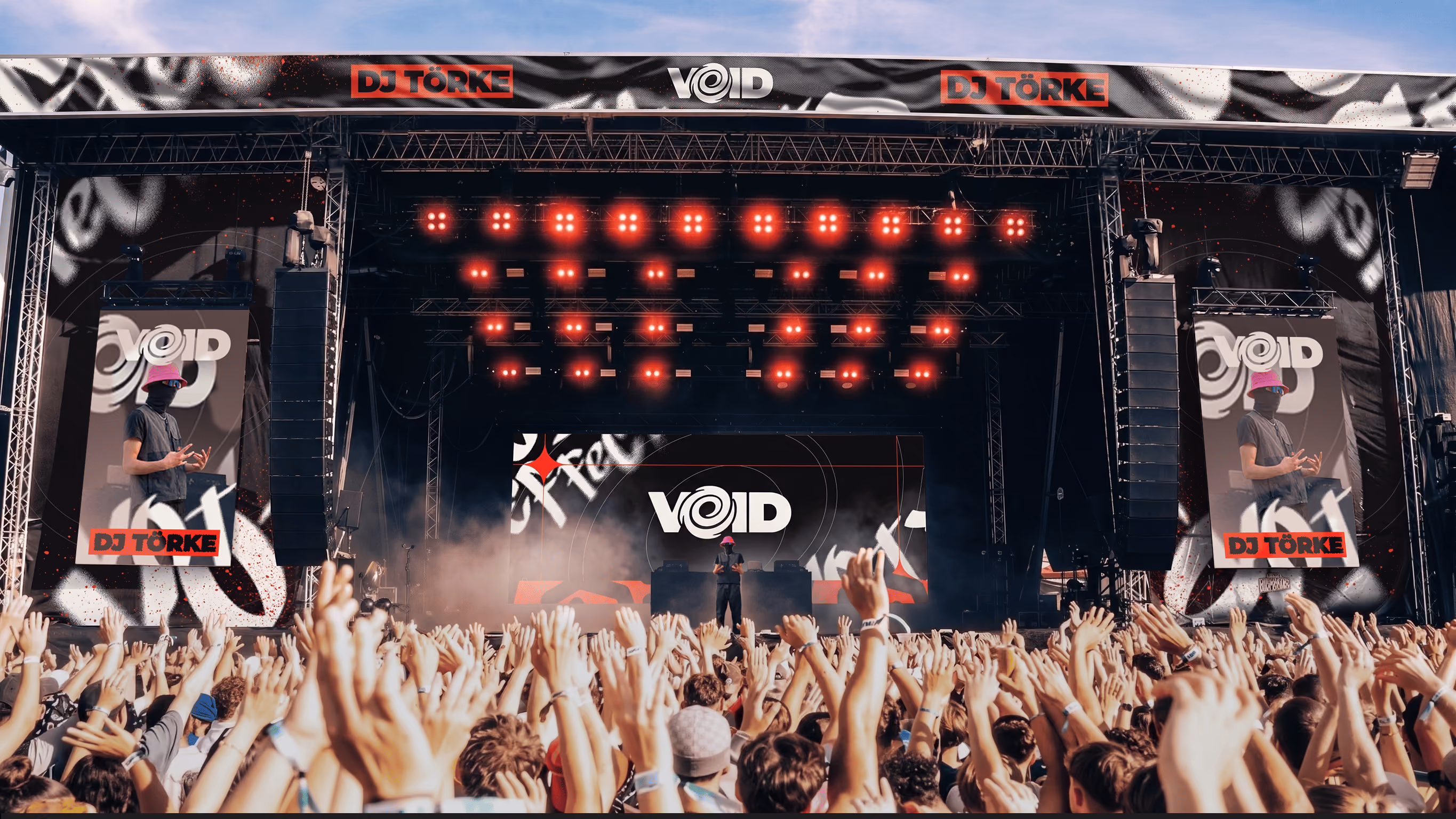 DJ wearing pink bucket hat performs on stage at crowded outdoor music festival with raised hands.