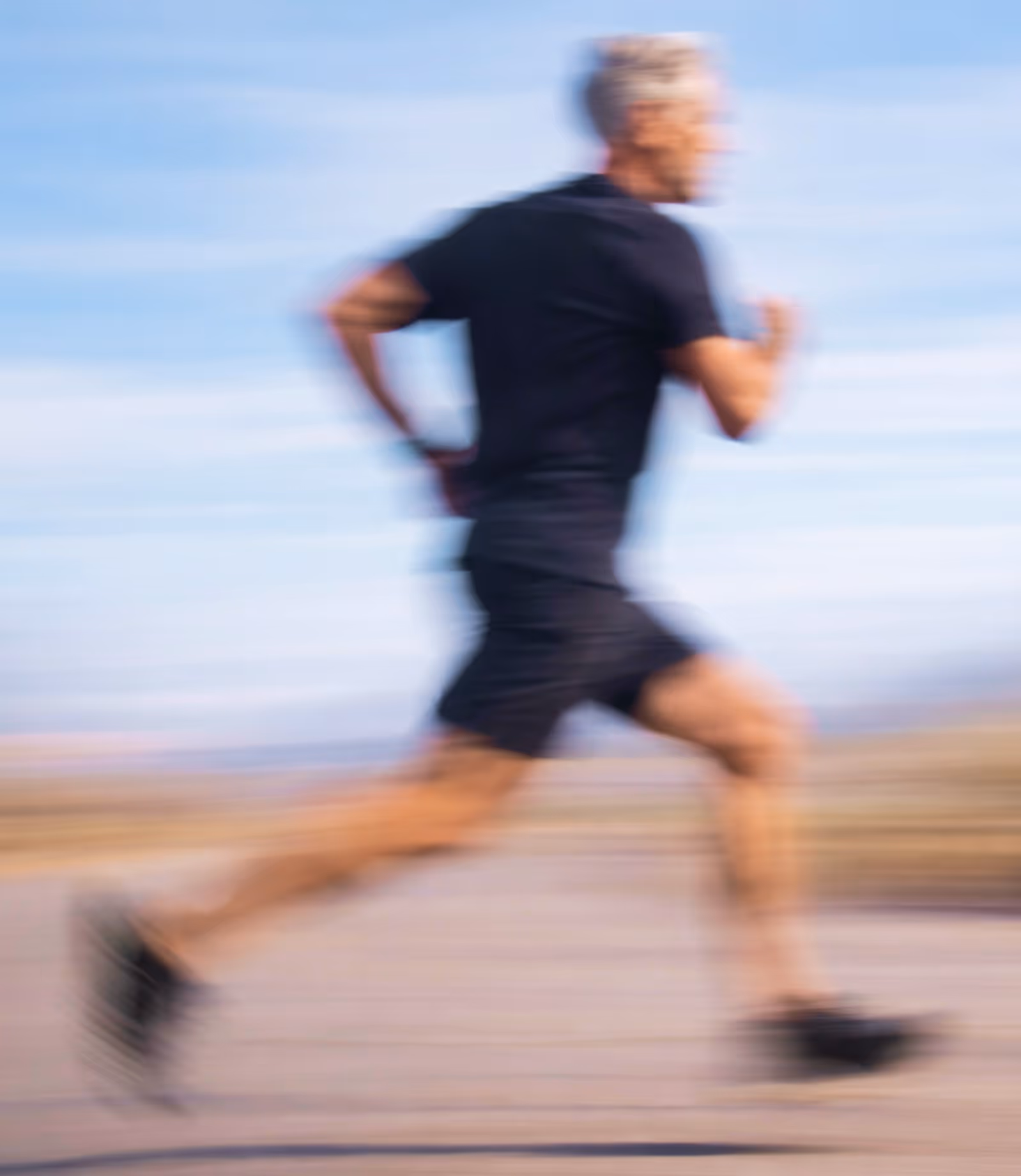 Smiling middle-aged man with gray hair and beard wearing glasses and a plaid shirt with backpack outdoors at sunset.