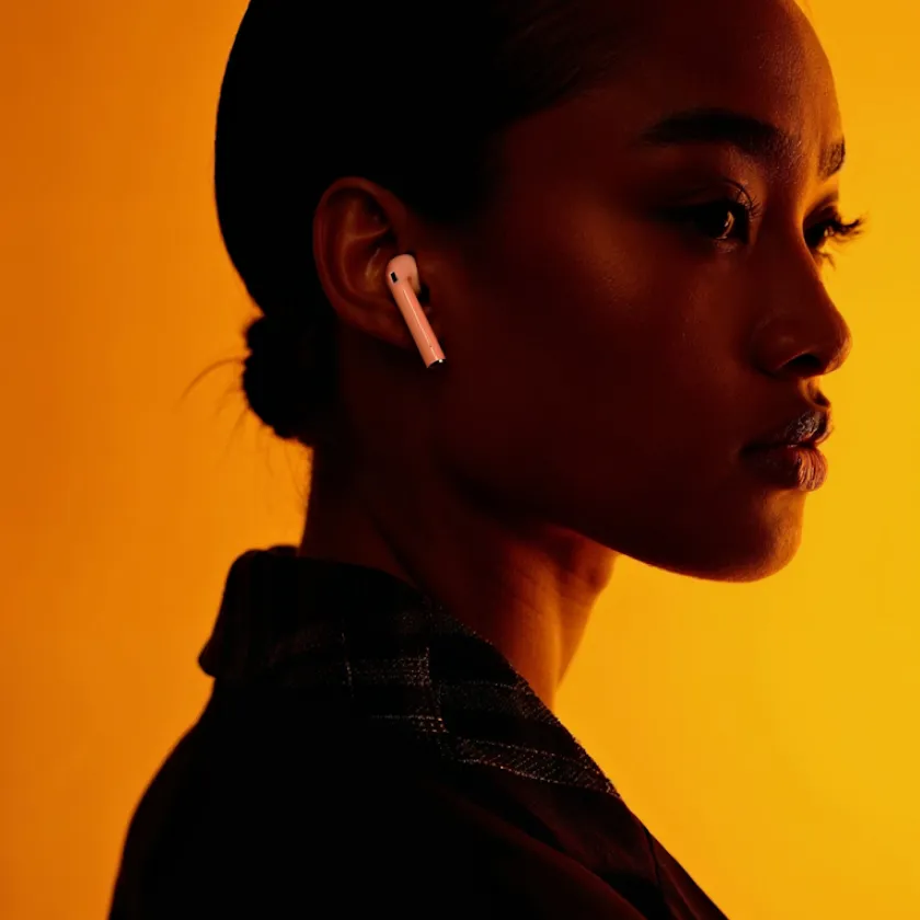 Side profile of a woman wearing wireless earbuds against an orange background.