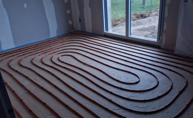 Installation de chauffage par le sol avec des tuyaux rouges disposés en serpentins dans une pièce en cours de construction.