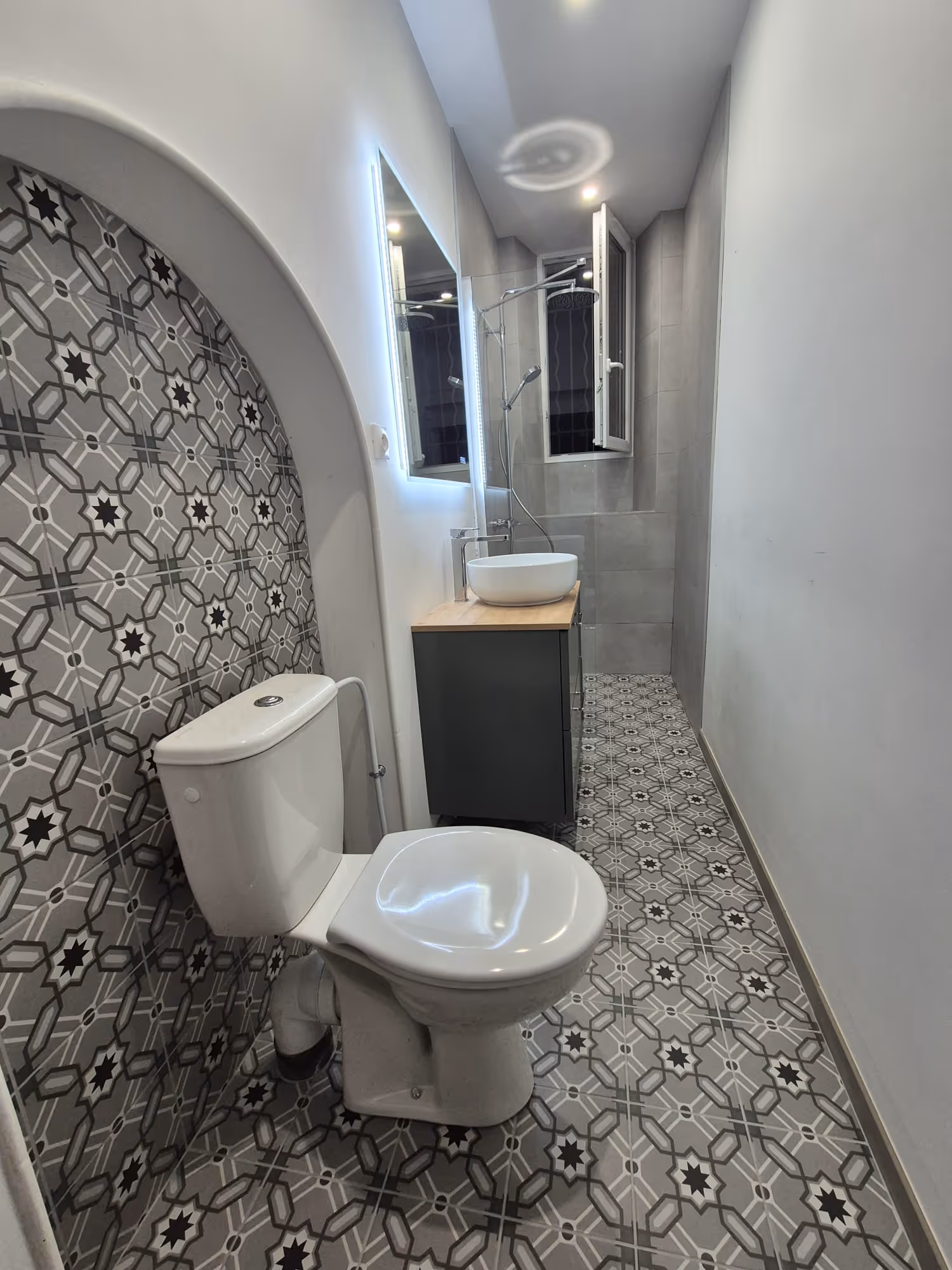 Douche moderne avec une paroi vitrée gravée de motifs géométriques sous une fenêtre de toit.