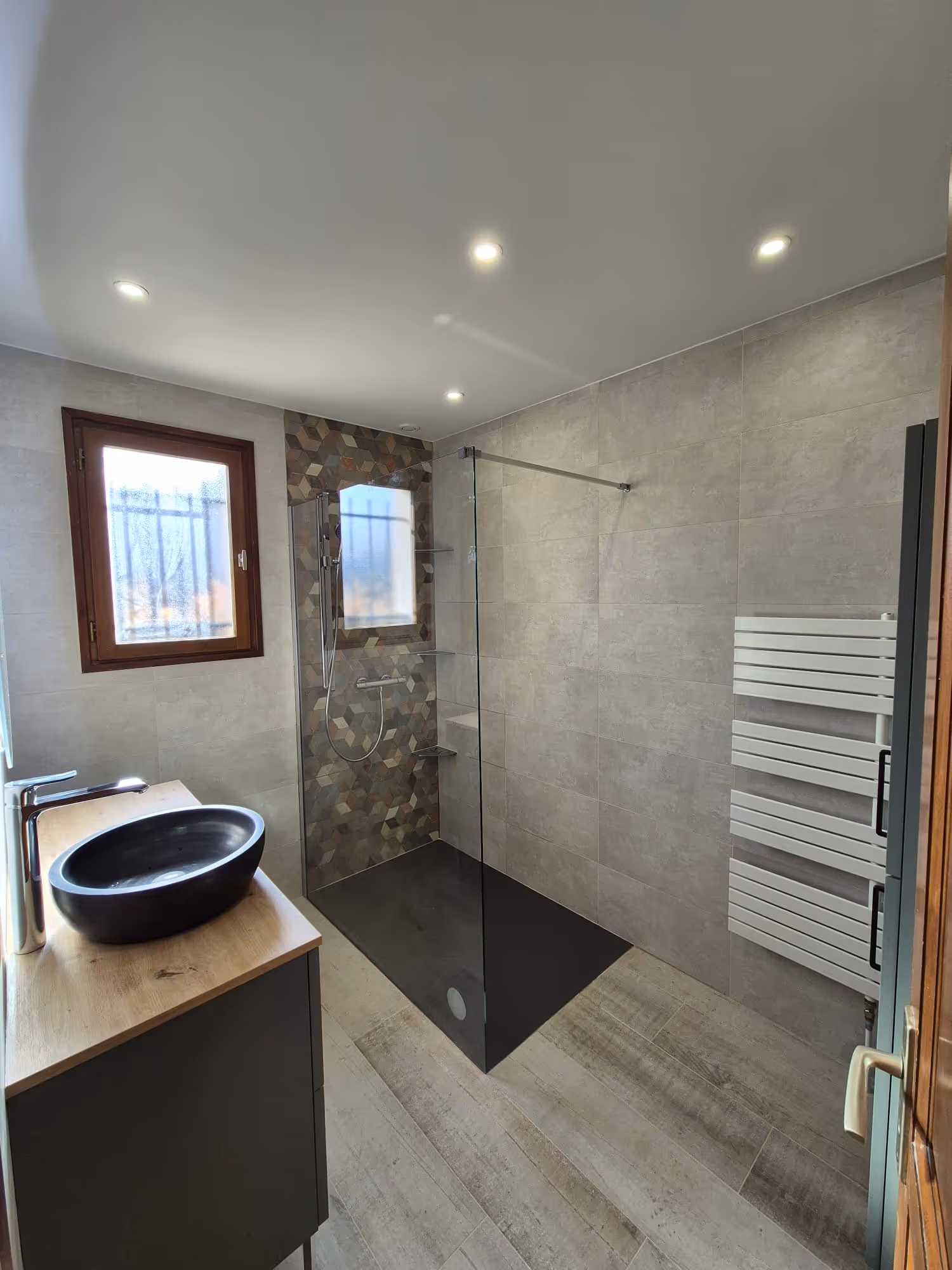 Douche moderne avec une paroi vitrée gravée de motifs géométriques sous une fenêtre de toit.