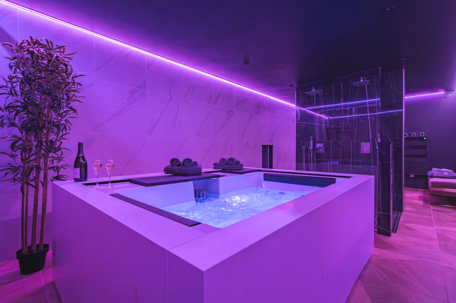 Salle de bain étroite avec toilettes blanches, lavabo sur meuble gris, douche à l'italienne et carrelage au sol et sur un mur en motifs géométriques gris, blanc et noir.