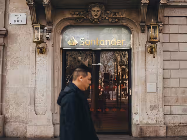 Fachada de edificio con balcón y persona caminando en calle urbana