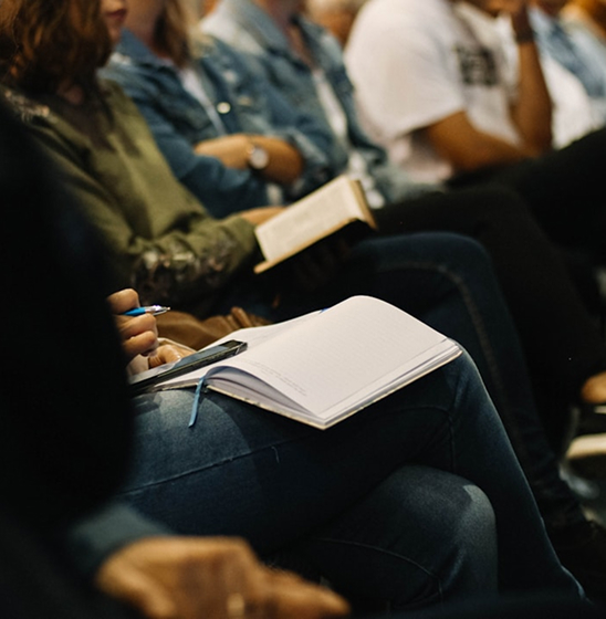 People seated at a professional meeting, taking notes during a presentation or group discussion.