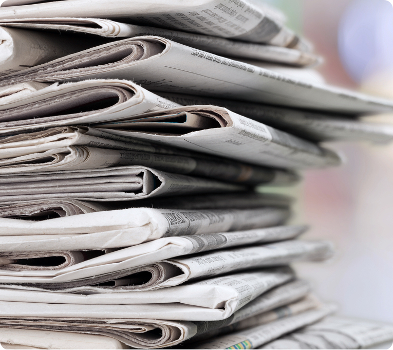 Stack of folded newspapers piled on top of each other, showing printed pages and headlines.
