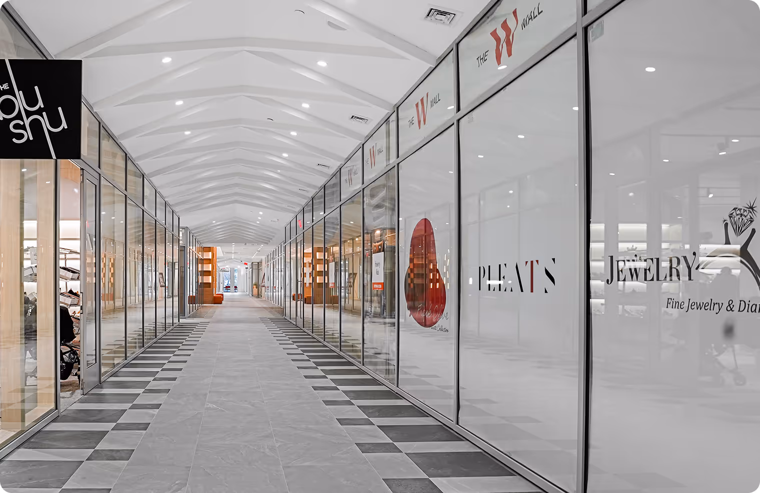 Empty modern shopping mall corridor with glass-fronted stores and a tiled floor.