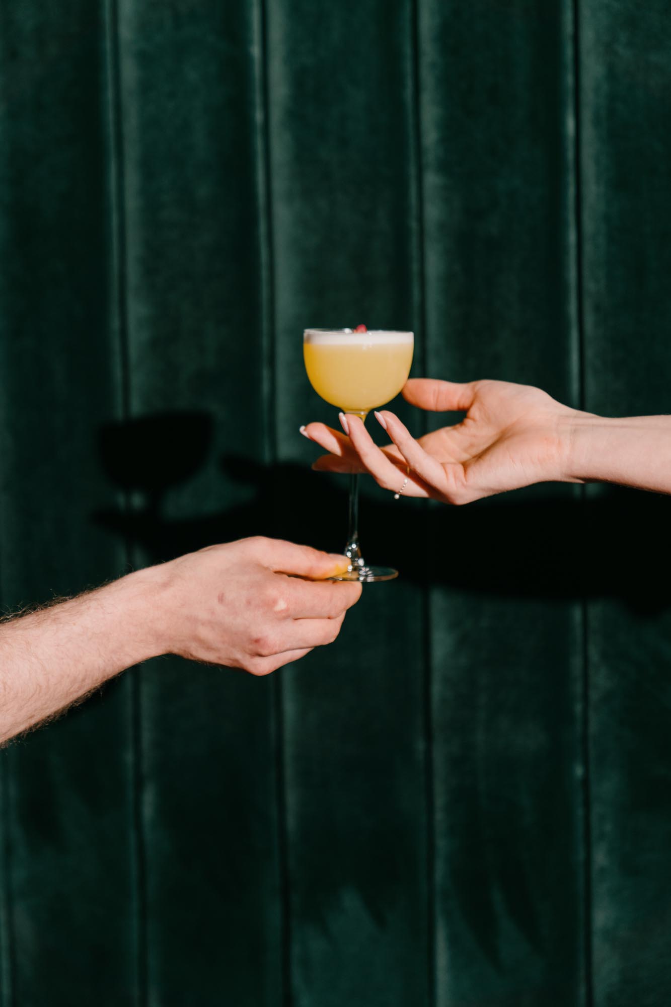 hands holding drinks against deep green curtain