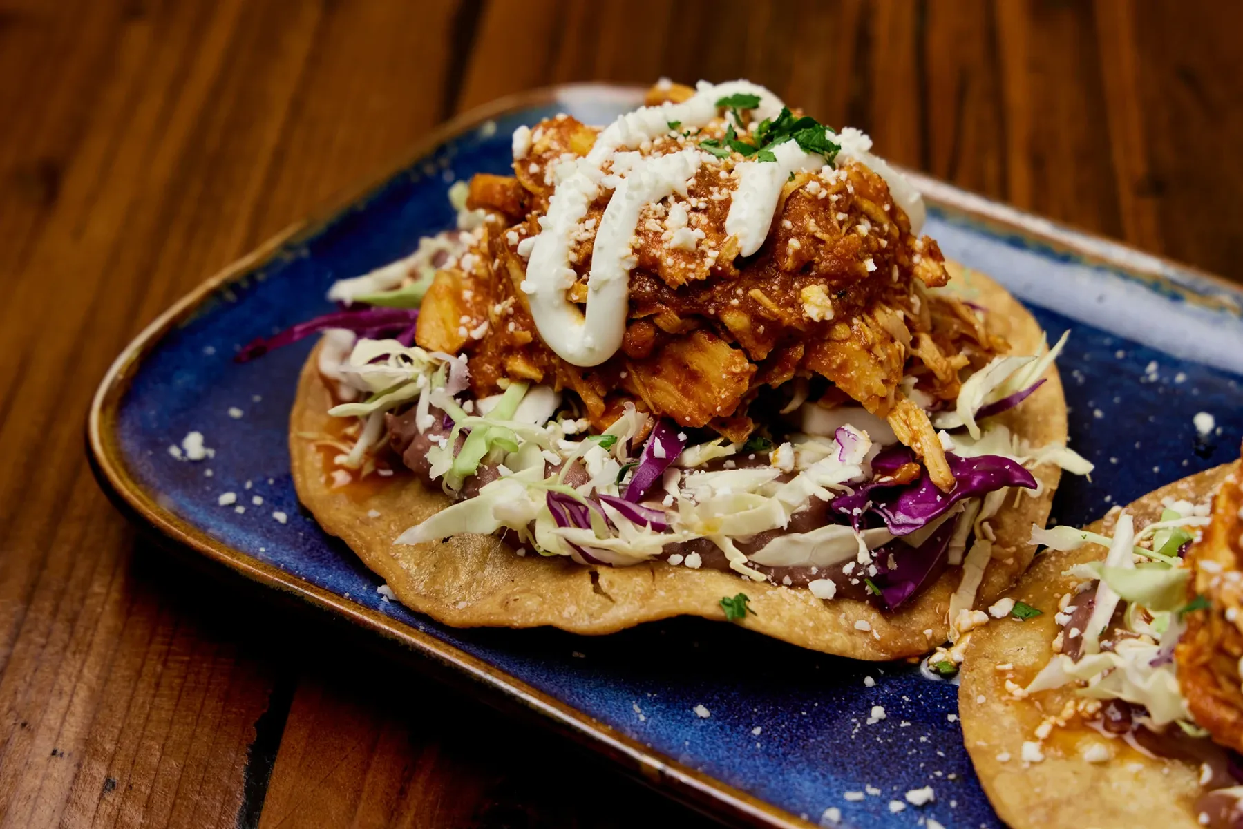 Tostada de Tinga: Corn tortilla chipotle stewed chicken, seda beans, cabbage, sour cream, queso fresco.