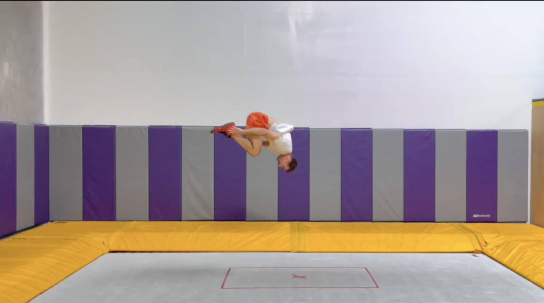 Female gymnast in a blue and black leotard performing a split leap mid-air during a competition.