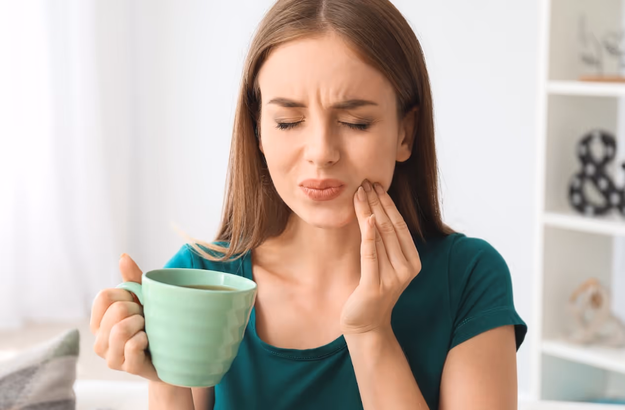 Woman reacting to tooth sensitivity while holding a warm beverage