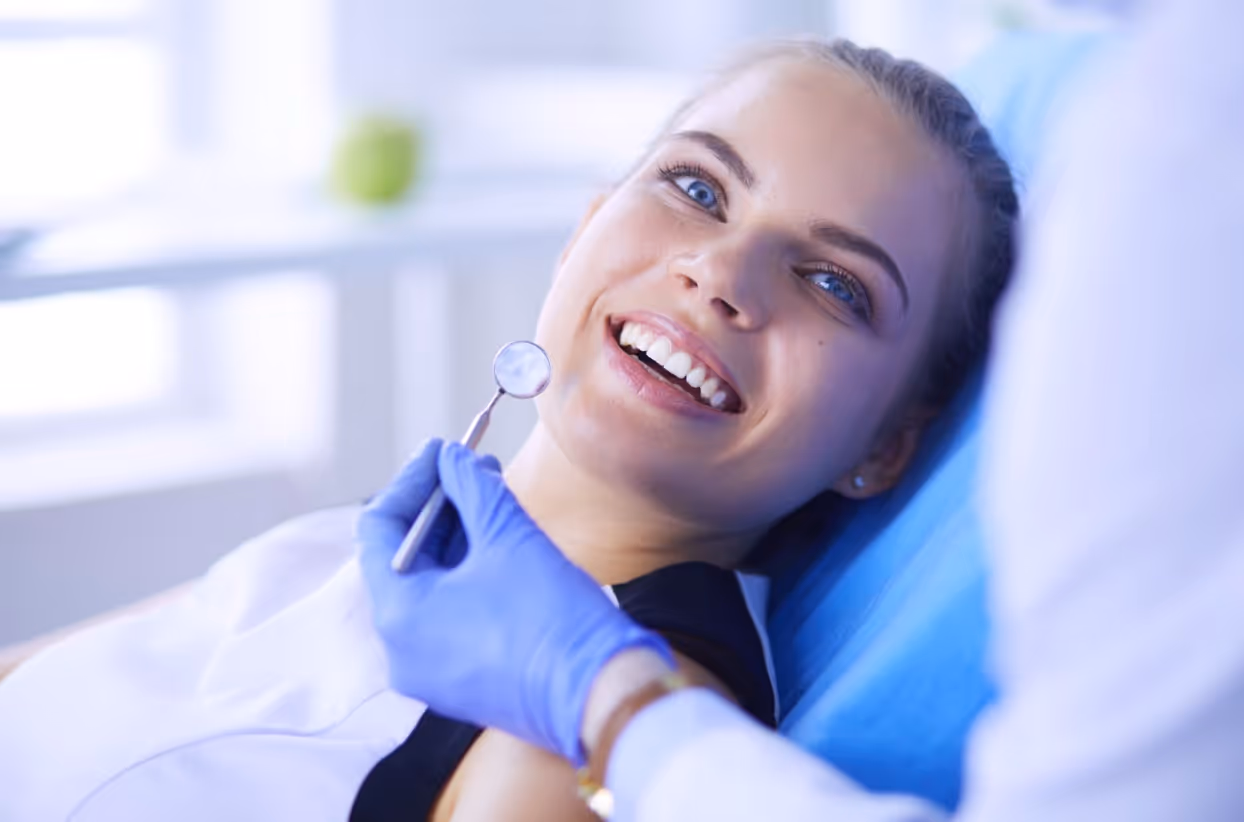 Woman smiling in a dental chair during an exam as the dentist prepares to check her teeth