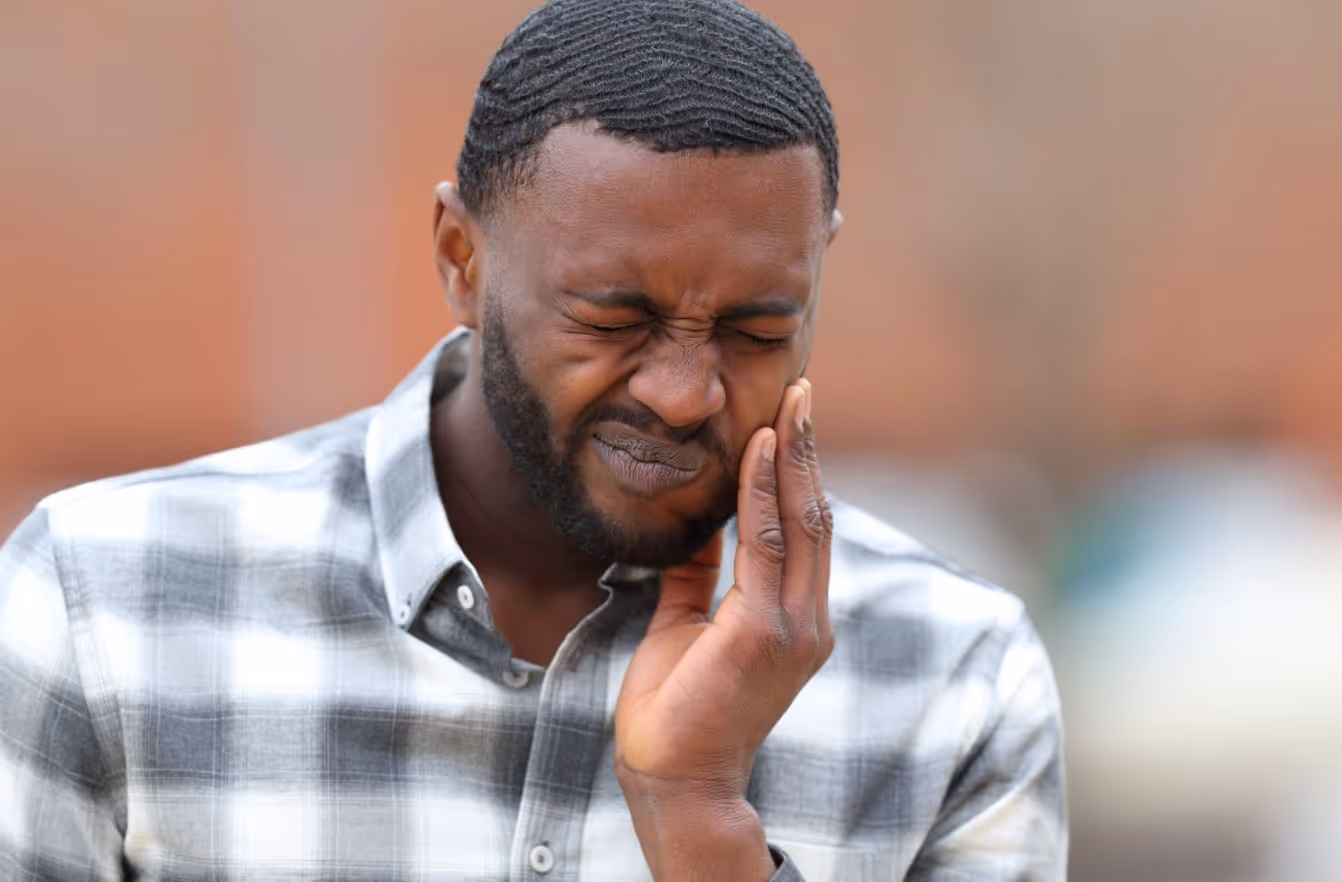 Man holding his cheek and wincing from sharp tooth pain outdoors