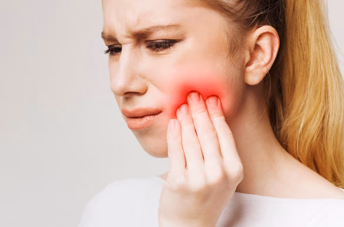 Woman touching her cheek with a painful expression and redness indicating tooth inflammation
