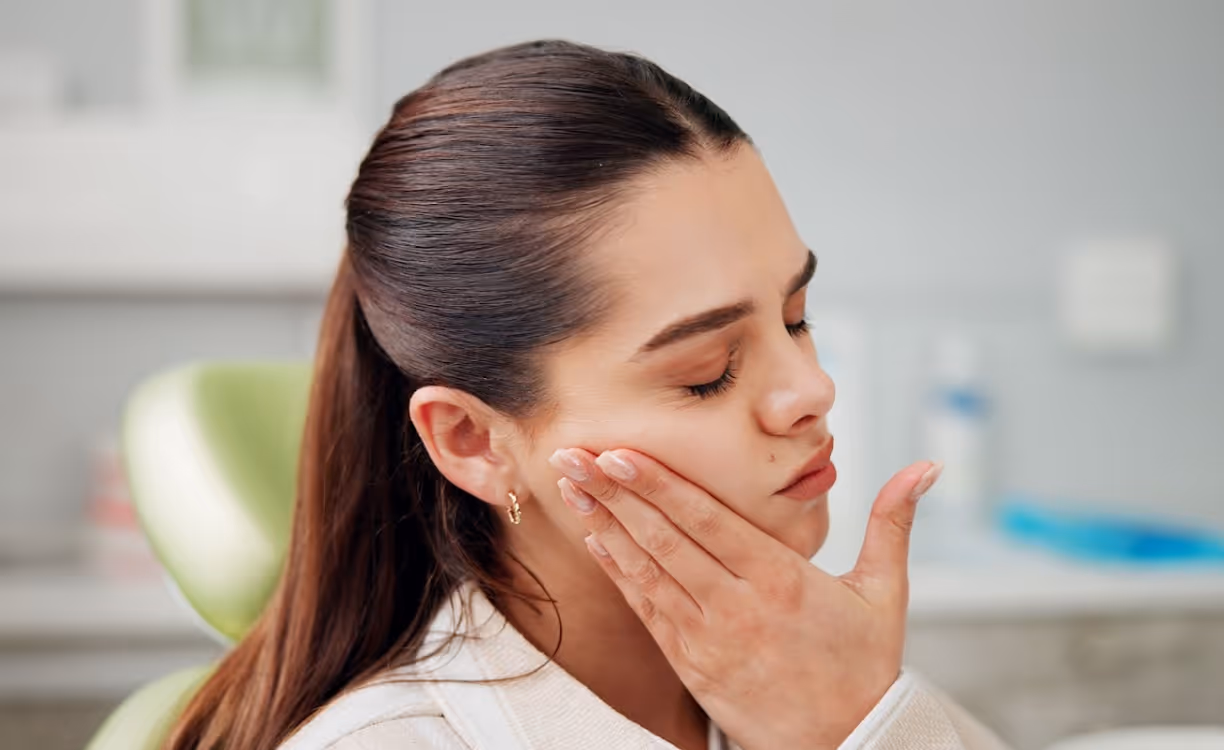 Woman touching her cheek while experiencing dental discomfort.