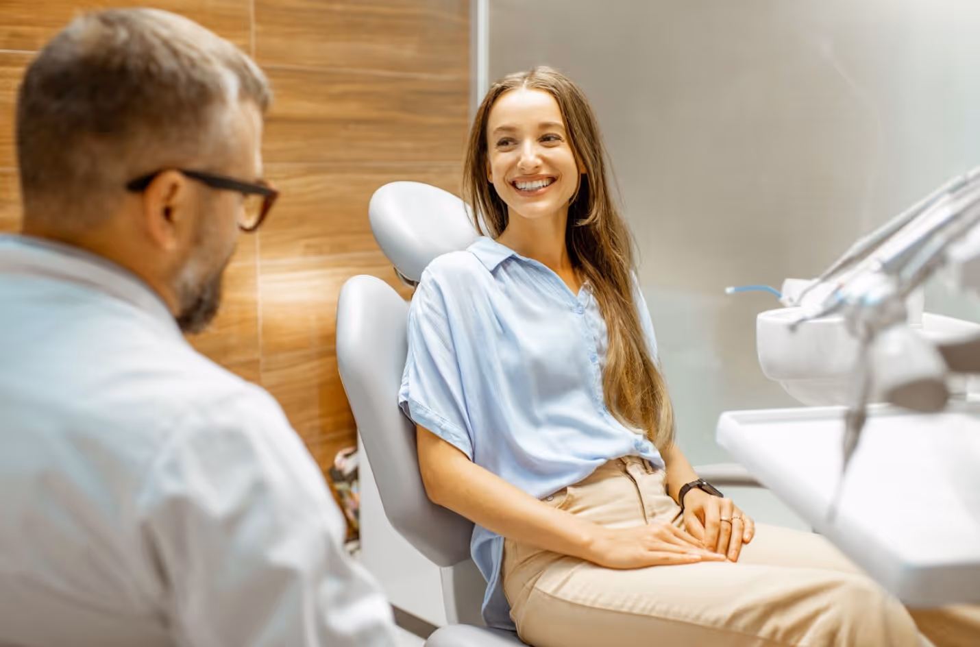 Woman smiling in a dental chair while talking with her dentist during a relaxed consultation.