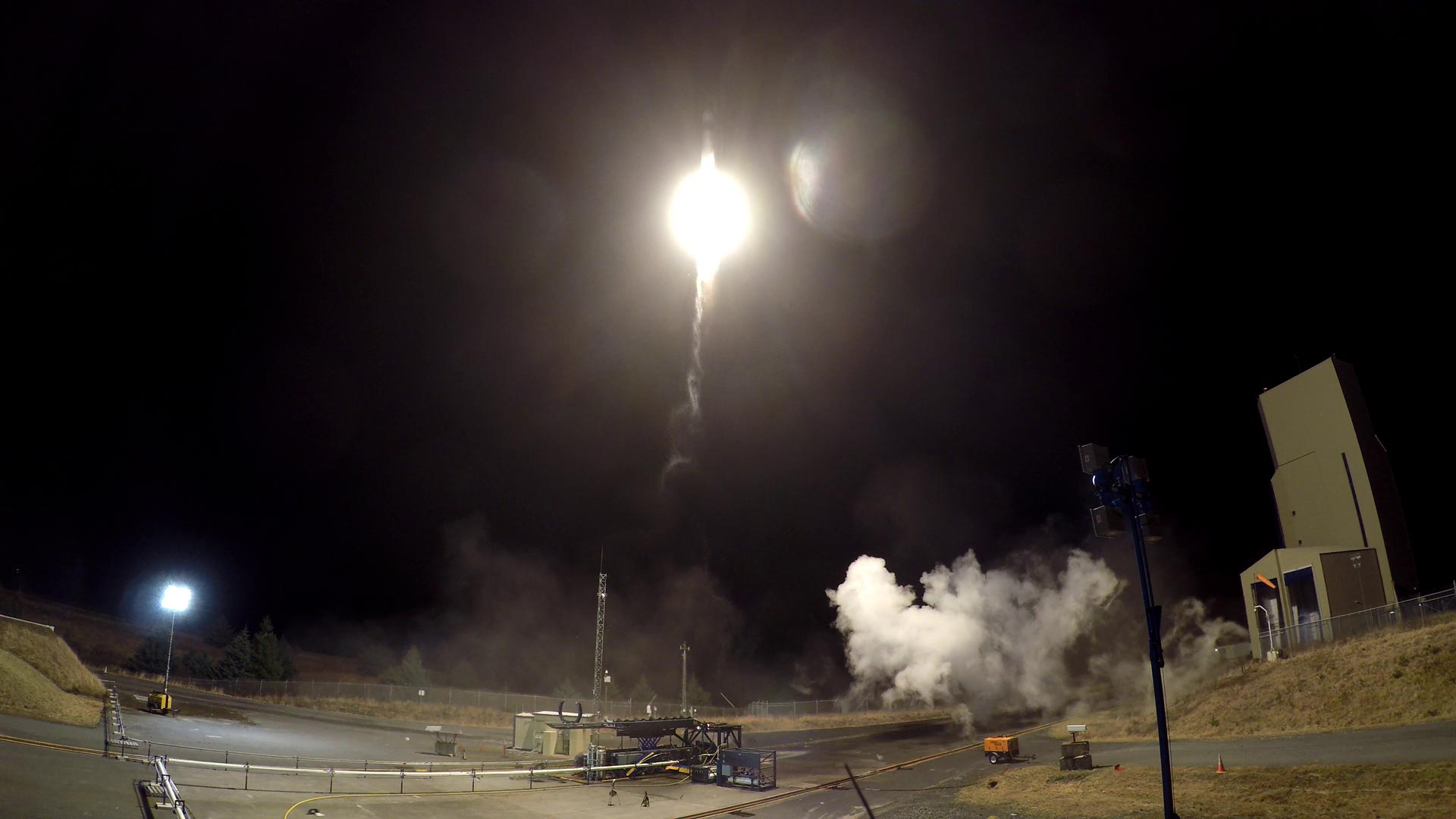 Bright rocket launch at night with smoke billowing near the launch pad.