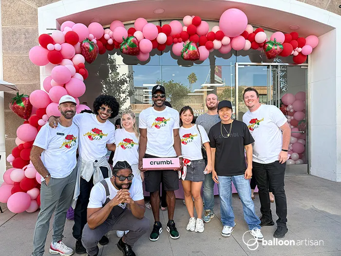 A custom strawberry themed balloon garland on a building for a Crumbl Cookie Grand Opening ribbon cutting celebration makes a stunning balloon photo op.