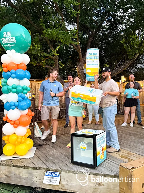 A balloon column tower with a branded logo balloon on it used as a balloon decoration at a company event photo moment.