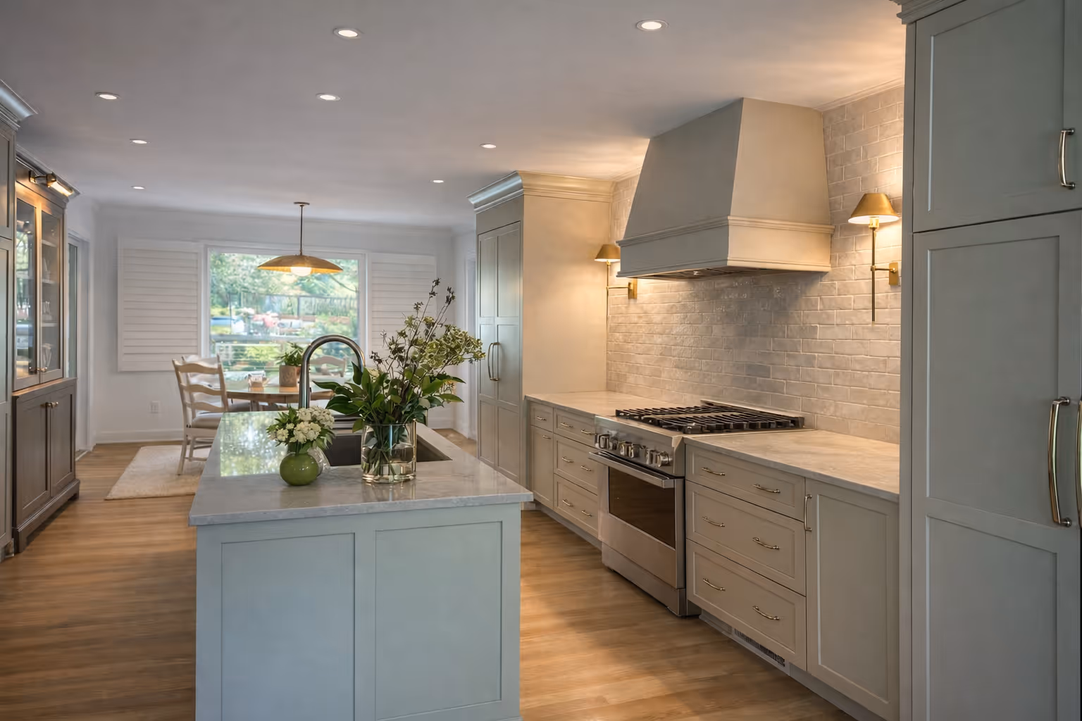 Bright modern kitchen with sage green shaker cabinets, marble island countertop, stainless steel gas range, white tile backsplash, and open dining area with garden view.
