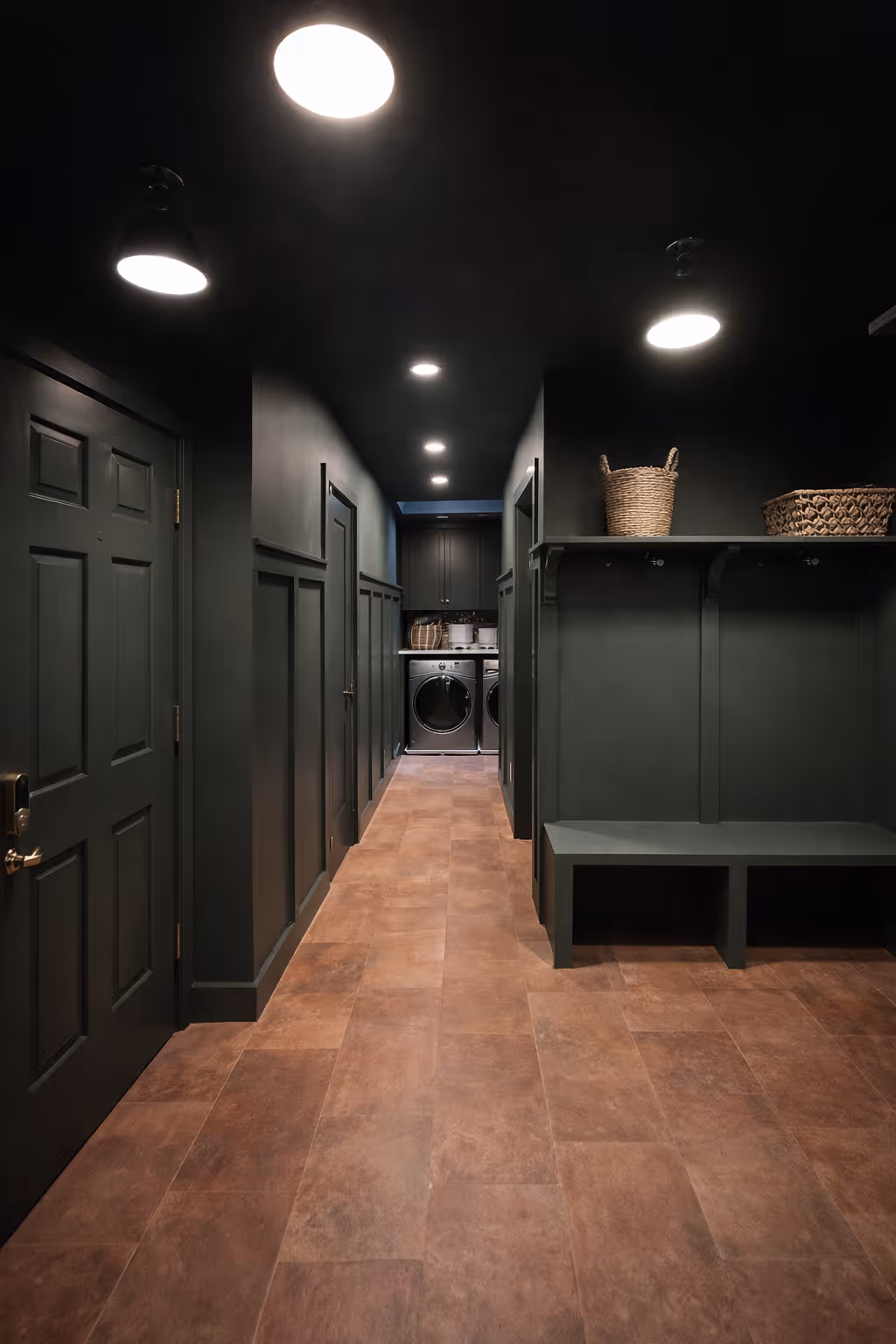 Dark green mudroom hallway with built-in bench and shelving, recessed lighting, tiled floor, and laundry area with washer and dryer at the end.