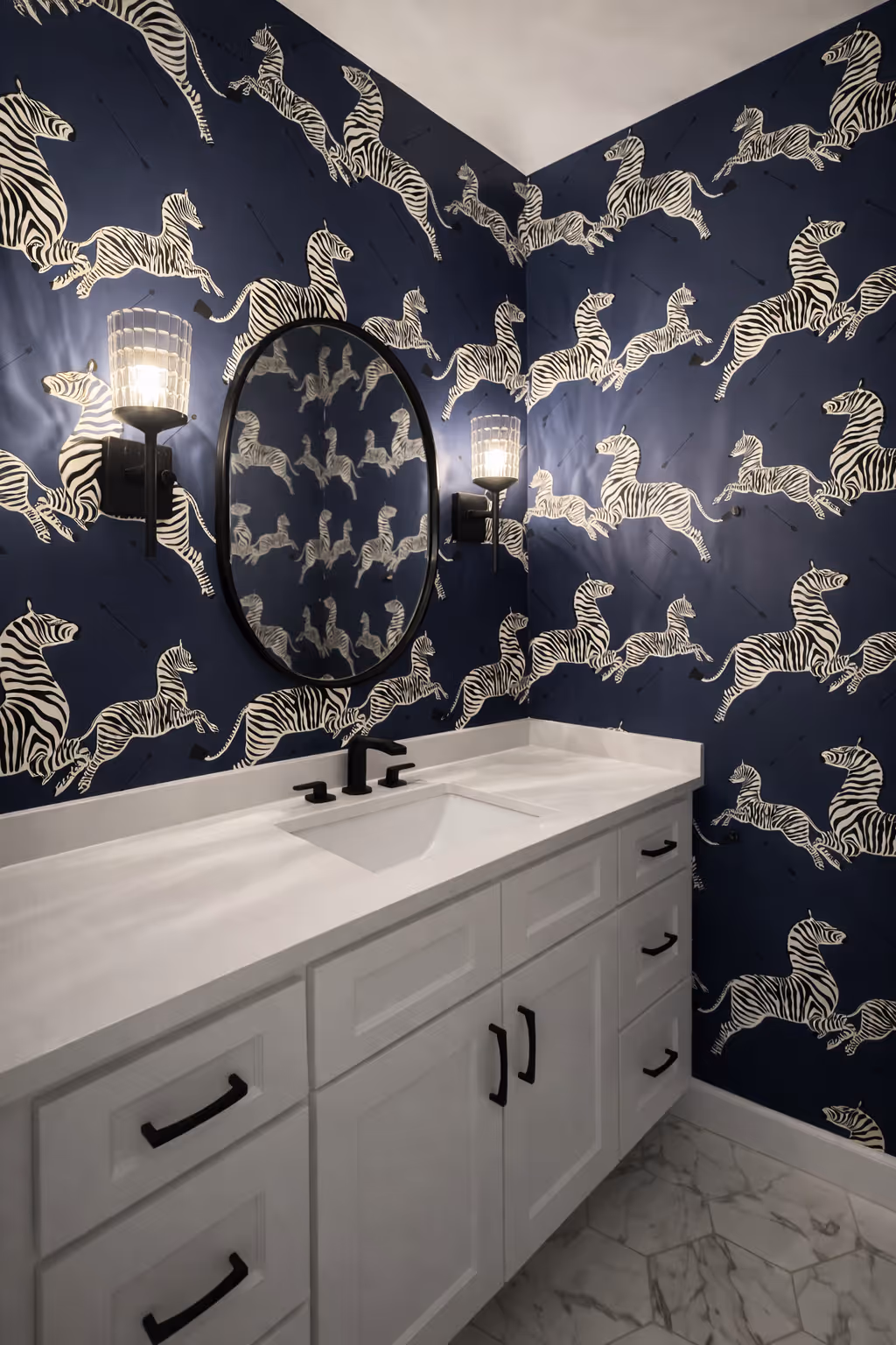 Bold powder room with navy zebra print wallpaper, white vanity, black faucet, oval mirror, and wall sconces.