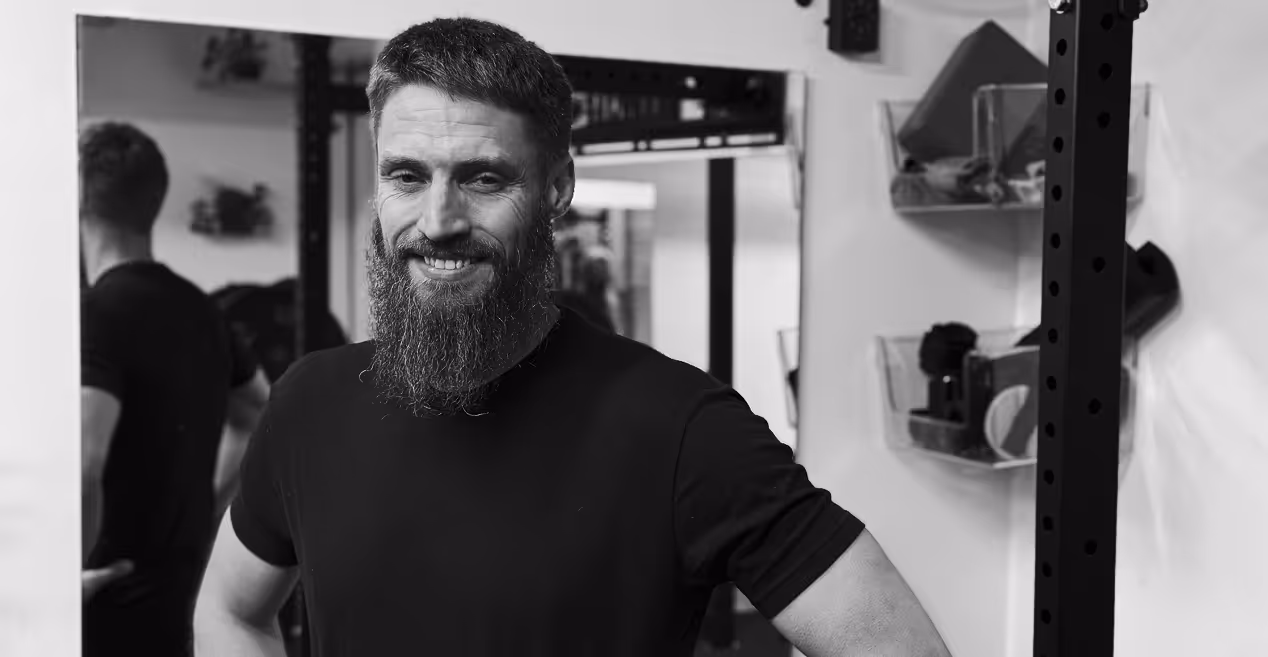 Paul Brownsberger, Owner of Holistic Resilience. Smiling man with beard and short hair standing confidently in a gym with hands on hips.