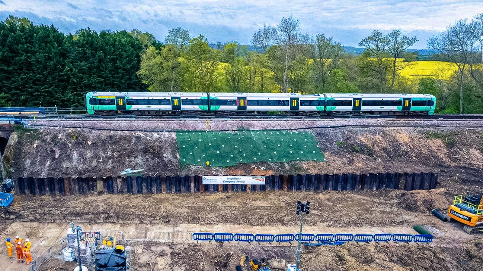 Green train passing over railway construction site with yellow field background