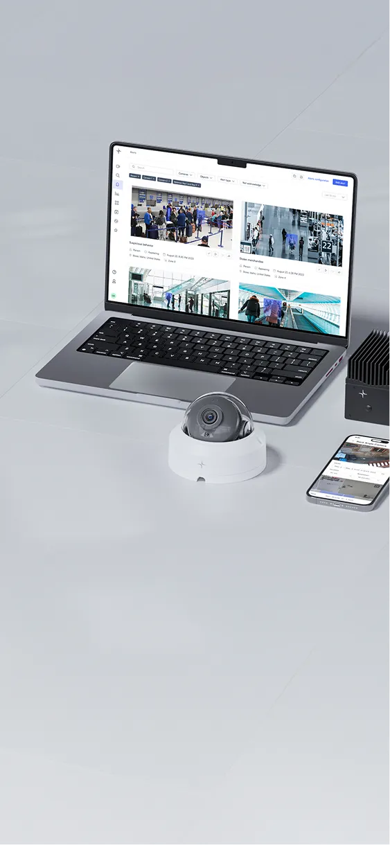 Laptop displaying security camera footage beside a dome security camera and a smartphone on a white surface.