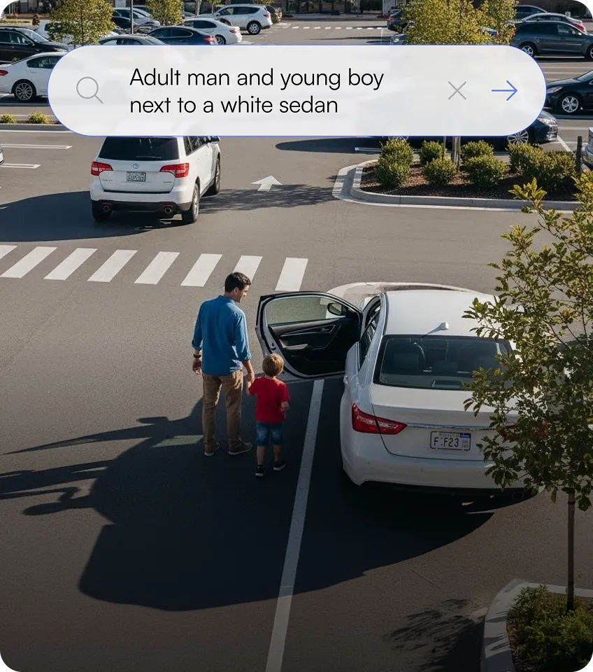Adult man and young boy standing next to an open door of a parked white sedan in a parking lot.