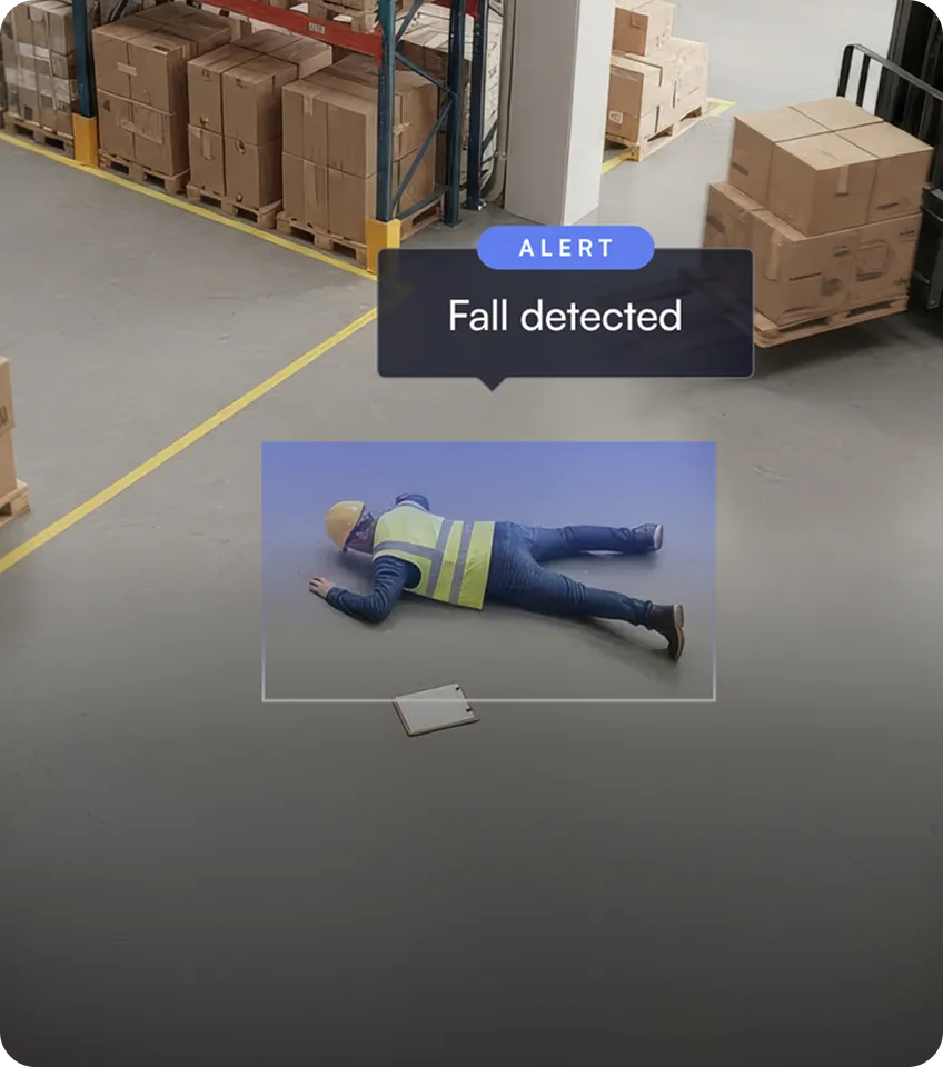 Worker wearing a safety vest and helmet lying on the floor of a warehouse with an alert reading 'Fall detected'.
