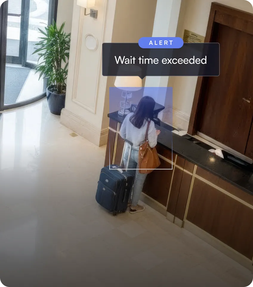 Woman with a suitcase and brown handbag standing at a hotel reception desk under a digital alert saying 'Wait time exceeded.'