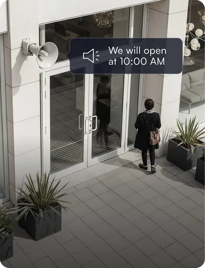 Person standing outside closed glass doors with a speaker sign displaying 'We will open at 10:00 AM'.