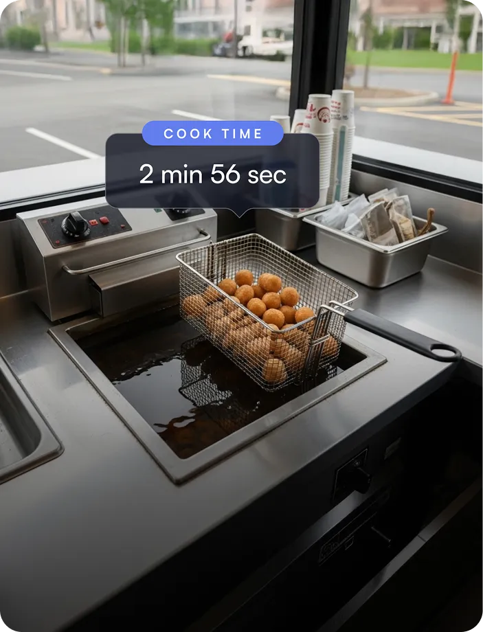 Metal fryer basket with small round fried food balls cooking in hot oil inside a commercial deep fryer with cook time displayed as 2 min 56 sec.