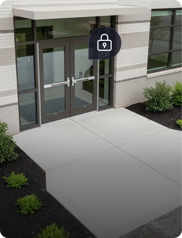 Closed double glass doors with metal push bars at a modern building entrance, with plants on either side and a lock icon overlay.
