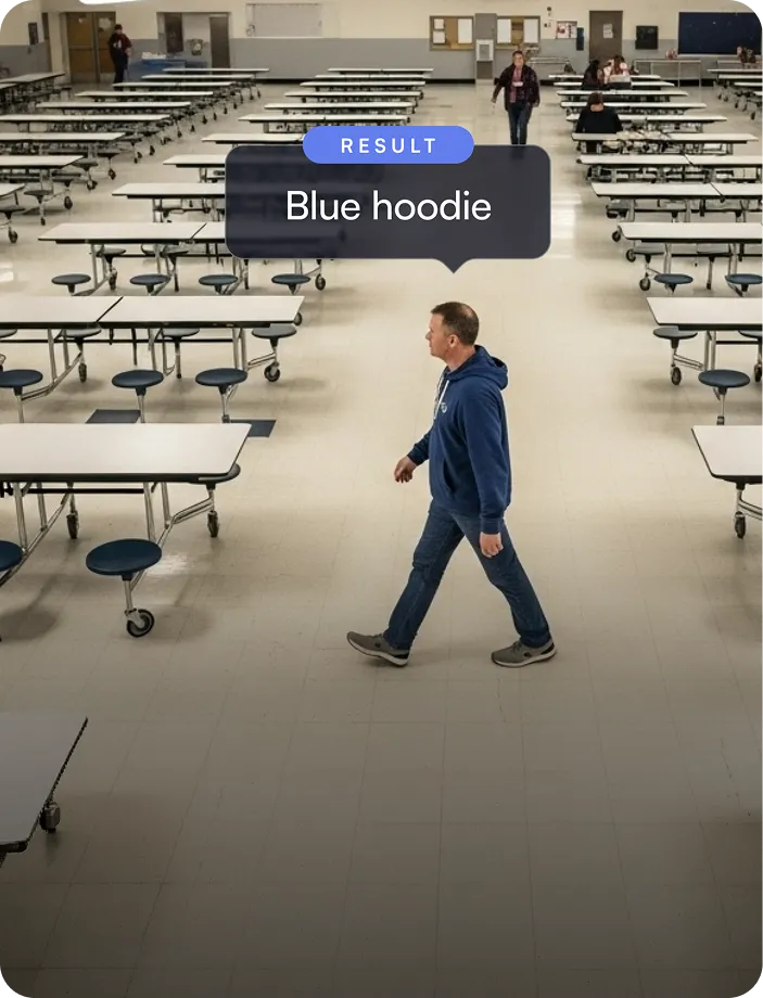 Man in blue hoodie walking across an empty cafeteria with rows of tables and chairs.
