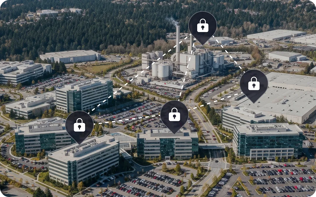 Aerial view of a corporate office park with several multi-story buildings, parking lots filled with cars, surrounded by forested hills; digital map markers with lock icons connected by dashed lines highlight certain buildings.