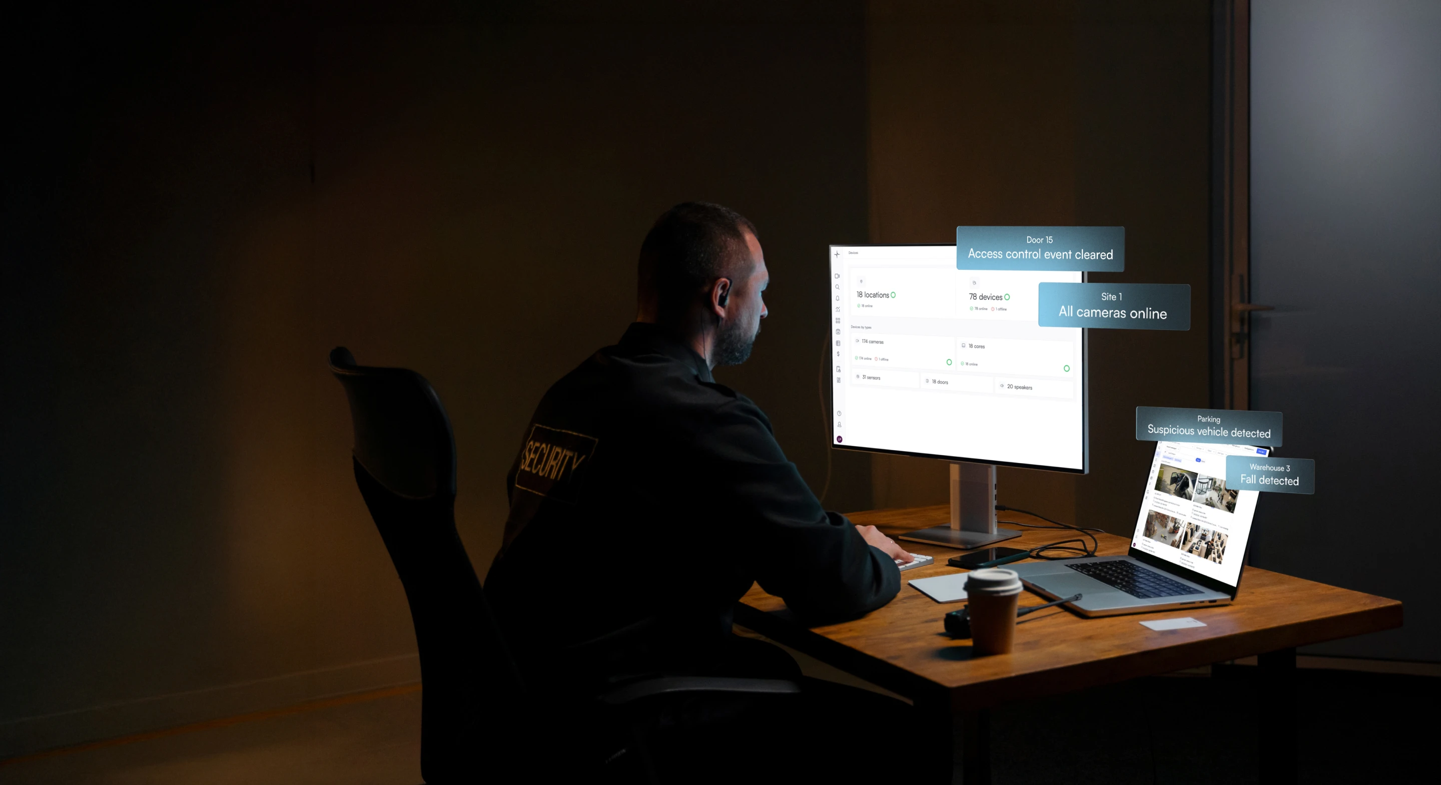Security guard monitoring multiple surveillance feeds and alerts on desktop and laptop screens in a dimly lit room.