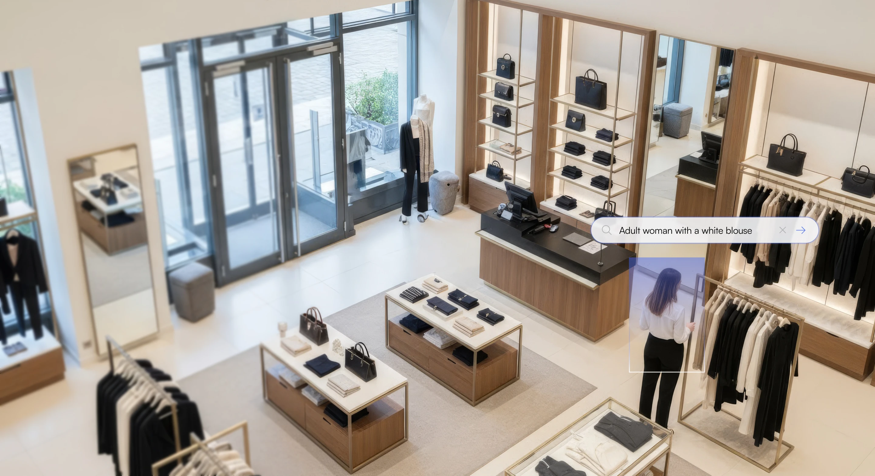 Modern clothing store interior with neatly arranged shelves and racks displaying bags and folded clothes, and a woman in a white blouse and black pants looking at a mirror.