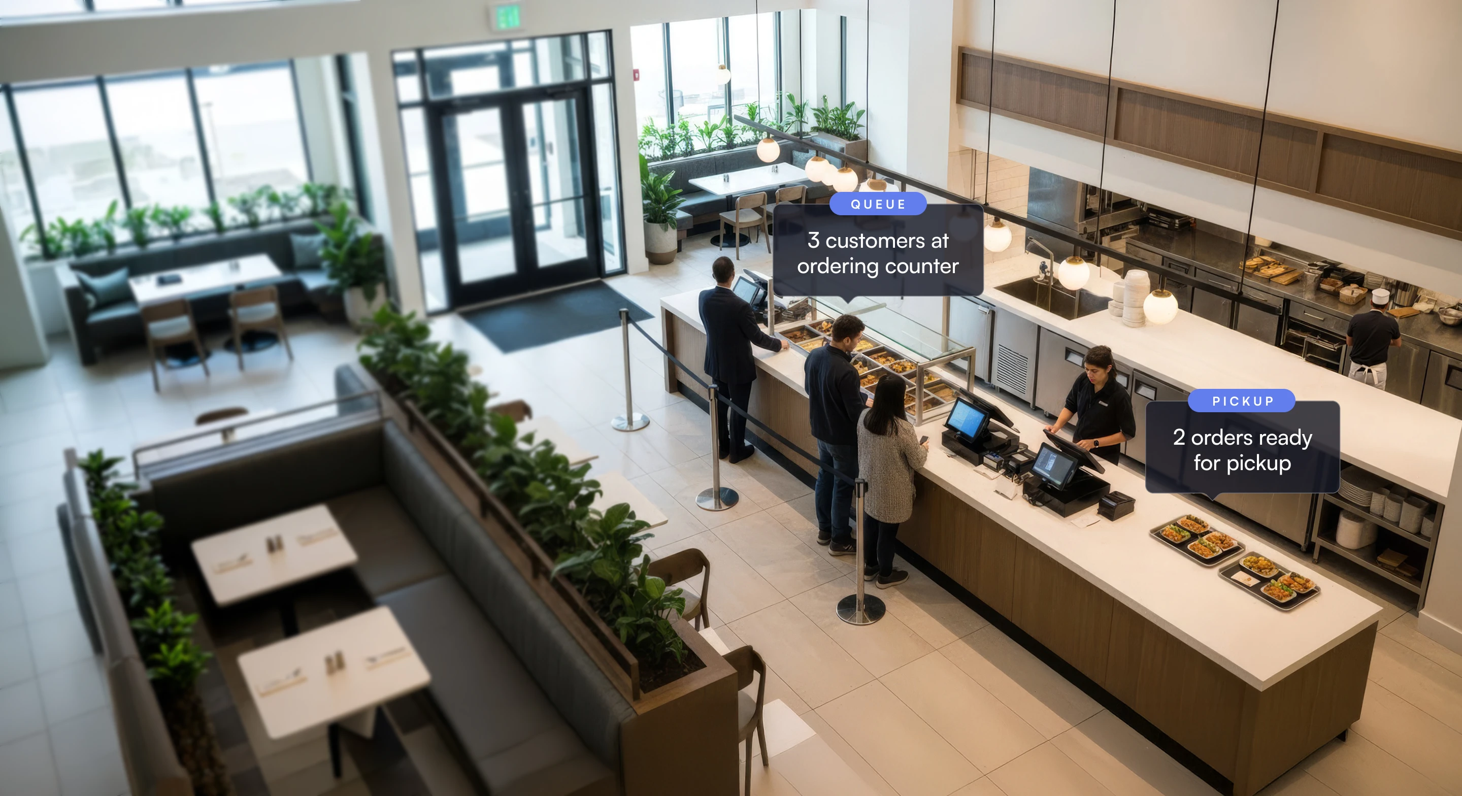 A modern cafeteria with three customers at the ordering counter and two food trays ready for pickup.
