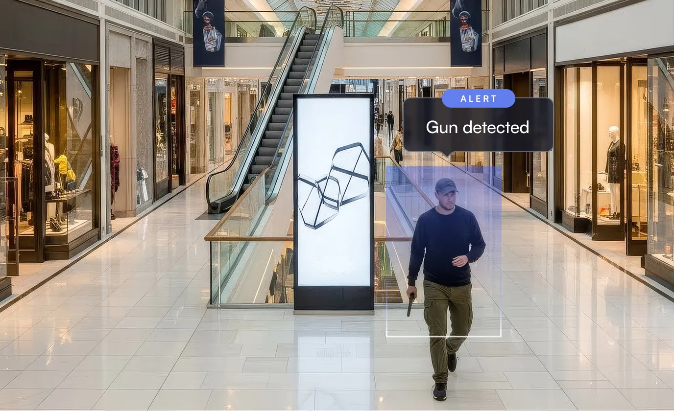 Man walking in a shopping mall holding a gun, with an alert box indicating 'Gun detected'.