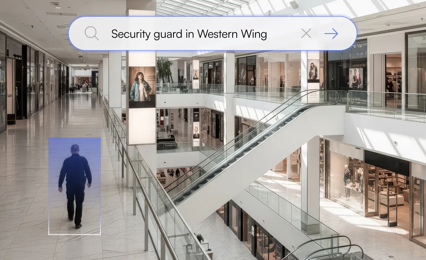 Security guard walking in spacious, modern shopping mall with escalators and glass railings.