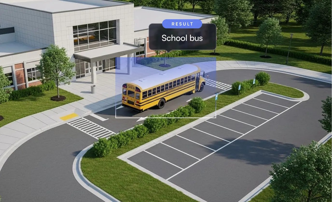 Yellow school bus driving on a curved driveway toward a school entrance with empty parking spaces nearby.